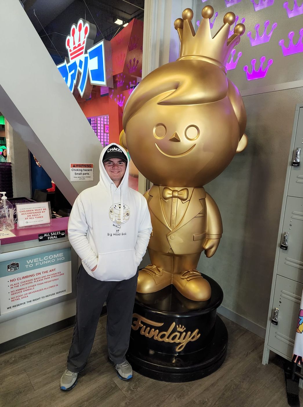 A fan in a white Big Head Bob hoodie next to a gold statue