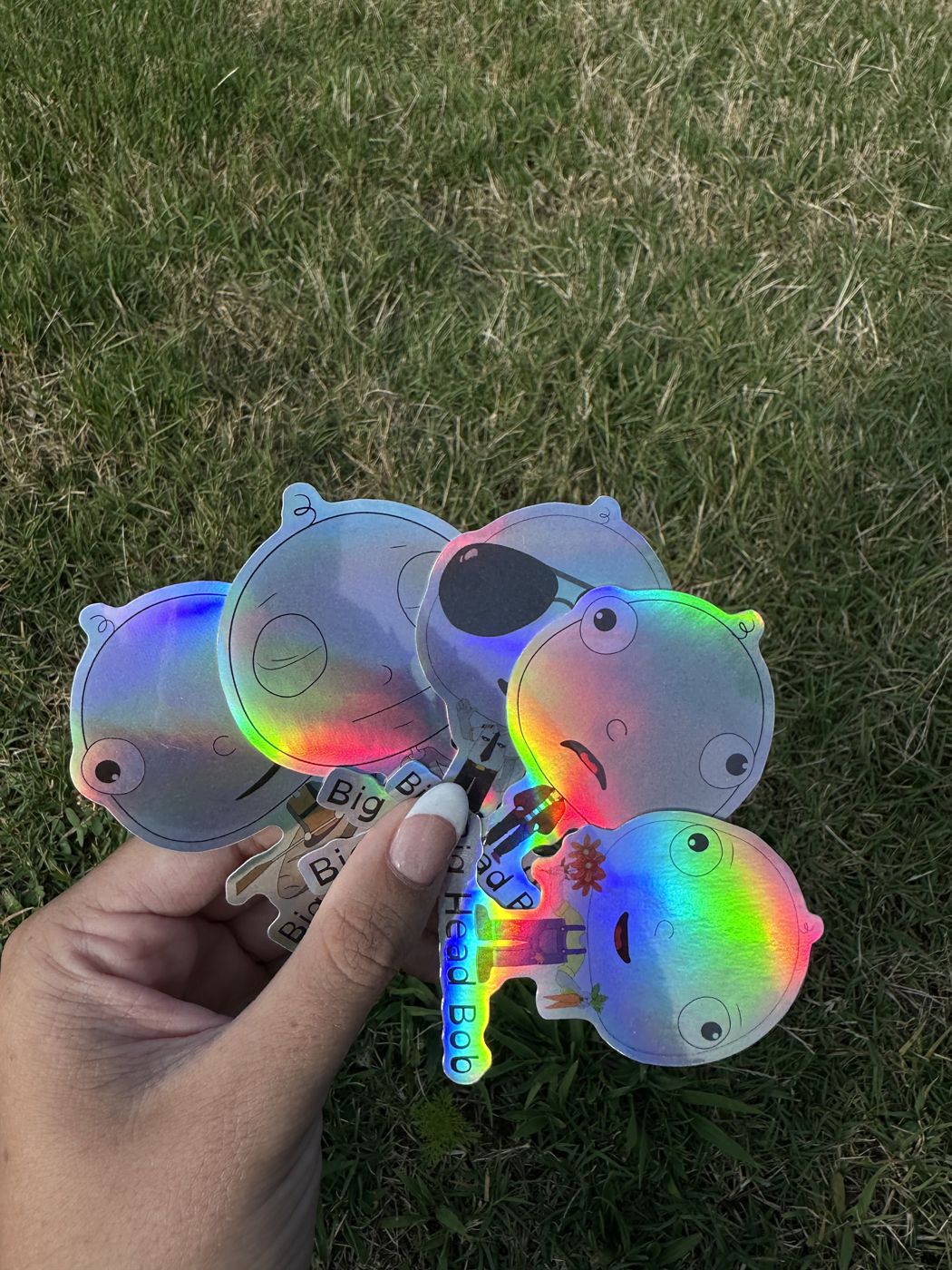 A hand holding holographic Big Head Bob stickers