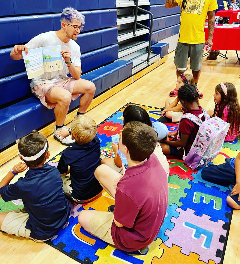 David Bradley reading a Big Head Bob book to students sitting on a gym floor