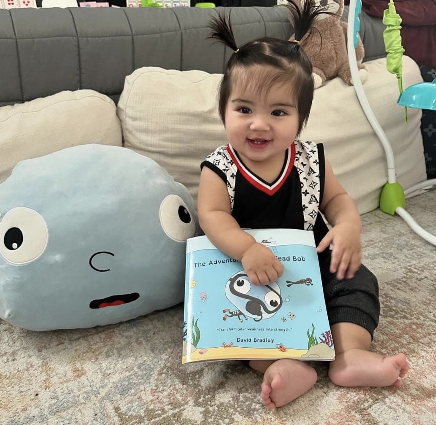 A baby holding the first Big Head Bob book next to a giant Bob plush