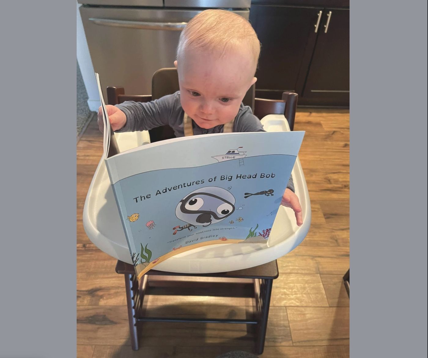 A baby in a high chair reading The Adventures of Big Head Bob