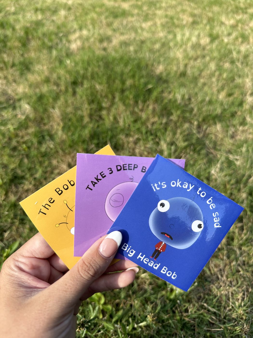 A hand fanning out Big Head Bob bookmarks